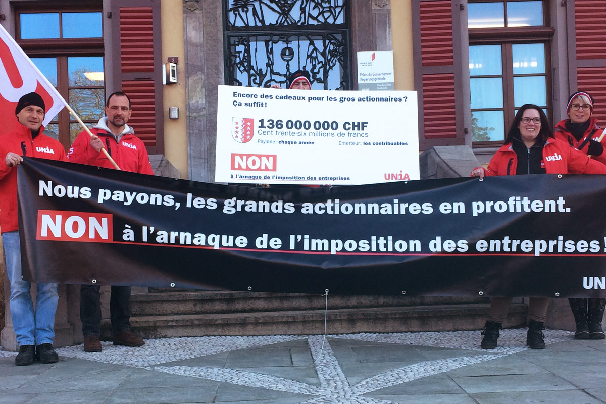 Militants d'Unia à Sion avec panneau: «(Drapeau valaisan)136'000'000 – Encore des cadeaux pour les gros actionnaires? ça suffit!»