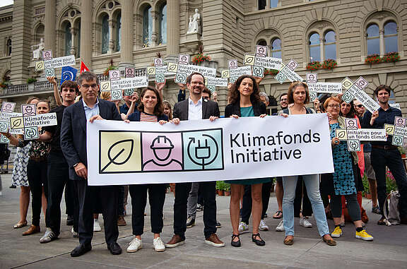 Des représentant-e-s du Parti socialiste, des Verts et Vertes et du syndicat Unia tiennent une banderole à l’effigie de l’initiative pour le fonds climat, devant le Palais fédéral.