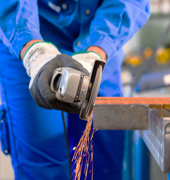 Una persona indossa guanti protettivi e lavora una griglia metallica con una smerigliatrice angolare, volano scintille.