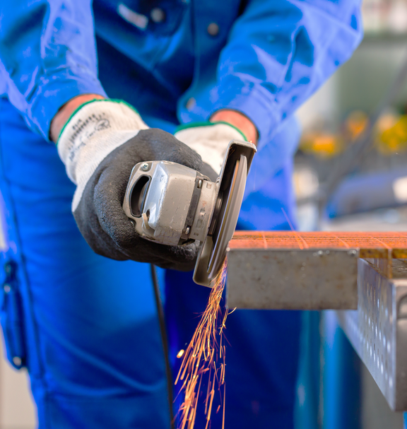 Une personne porte des gants de protection et travaille un treillis métallique avec une meuleuse d’angle, des étincelles jaillissent.