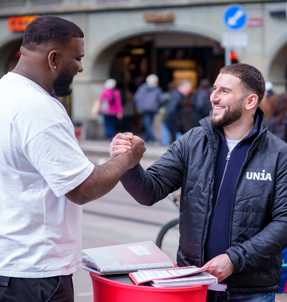 Unia-Dialoger im Gespräch mit einem Passanten, beide reichen sich lachend die Hand.