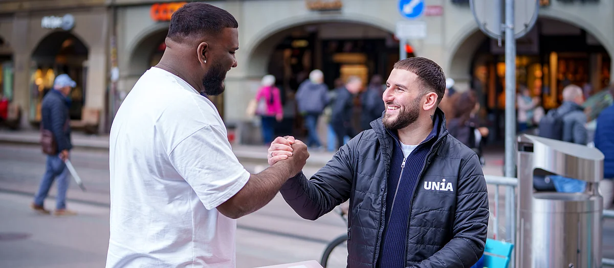 Unia-Dialoger im Gespräch mit einem Passanten, beide reichen sich lachend die Hand.