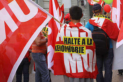 Dans une manifestation, un homme porte un drapeau contre la xénophobie sur le dos.