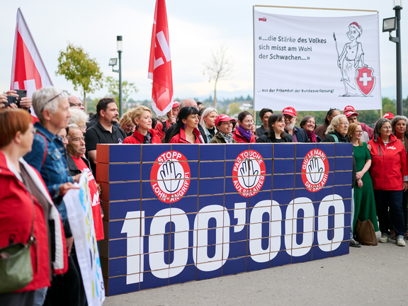 Unia e altre organizzazioni consegnano alla Cancelleria federale circa 100'000 firme contro l'attacco ai salari minimi. Al centro della scena c'è un grande muro di cartone su cui è scritto il numero «100'000».