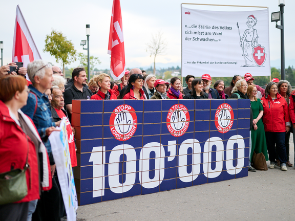 Avec d'autres organisations, Unia remet à la Chancellerie fédérale 100 000 signatures contre l'attaque sur les salaires minimums, contenues dans plusieurs cartons constituant un mur sur lequel figure le nombre 100 000.