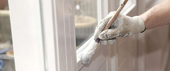 Mano di un pittore con guanto bianco dipinge il telaio di una finestra di colore bianco