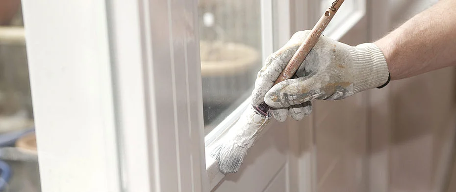 Hand eines Malers mit weissem Handschuh streicht einen Fensterrahmen mit weisser Farbe