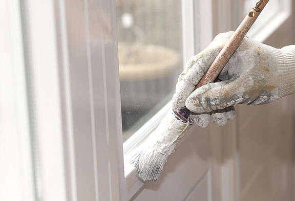 Mano di un pittore con guanto bianco dipinge il telaio di una finestra di colore bianco