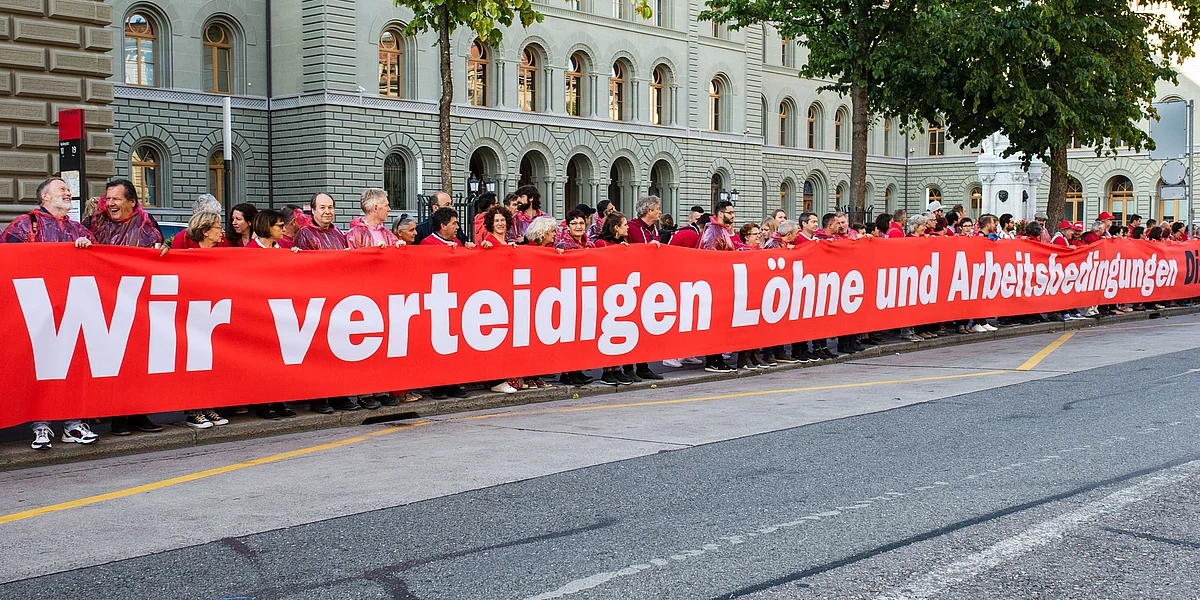 Eine lange Menschenkette demonstriert mit einem grossen roten Transparent mit der Aufschrift «Wir verteidigen Löhne und Arbeitsbedingungen» für starke Arbeitsrechte im Rahmen der Schweiz-EU-Beziehungen.