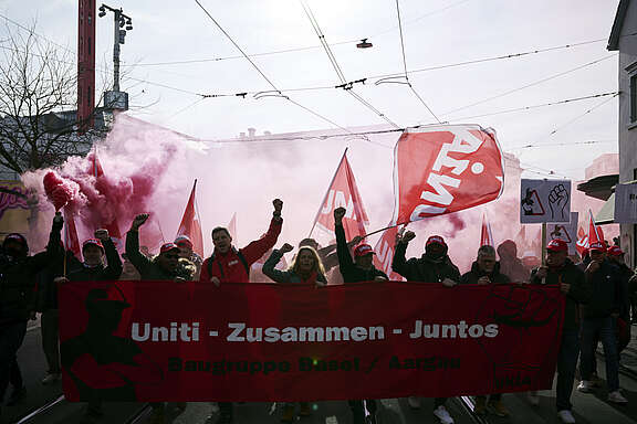 Des personnes manifestent avec des drapeaux rouges et une bannière «Uniti – Zusammen – Juntos» dans une rue de la ville.