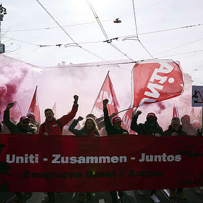 Des personnes manifestent avec des drapeaux rouges et une bannière «Uniti – Zusammen – Juntos» dans une rue de la ville.