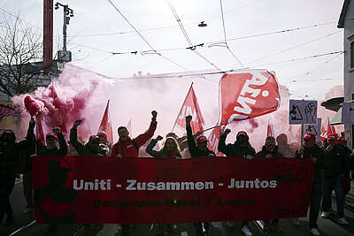 Des personnes manifestent avec des drapeaux rouges et une bannière «Uniti – Zusammen – Juntos» dans une rue de la ville.