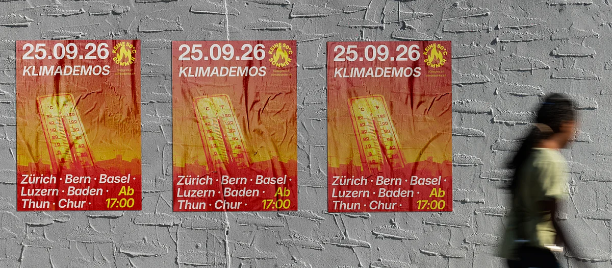 Drei Plakate mit der Aufschrift «25.09.26 – Keine 50°C Sommer» hängen an einer grauen Backsteinwand, während zwei Passant:innen vorbeigehen.