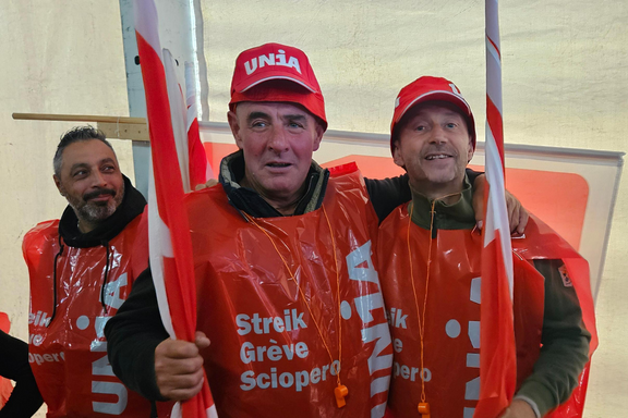 Trois travailleurs de la construction sont vêtus de la tête au pied avec du matériel du syndicat Unia