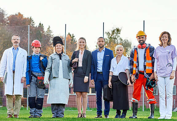 Huit personnes en habits de travail typiques des branches représentées par le syndicat Unia se tiennent l'une à côté de l'autre.