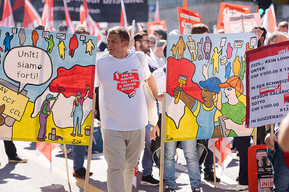 Manifestazione di pittori e stuccatori con striscioni e manifesti. I manifestanti chiedono migliori condizioni di lavoro e salari minimi. Due cartelli colorati mostrano i lavoratori con slogan.