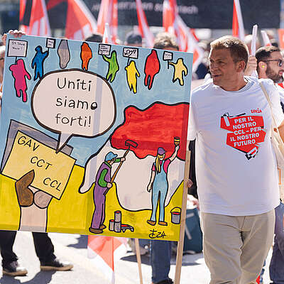 Manifestazione di pittori e stuccatori con striscioni e manifesti. I manifestanti chiedono migliori condizioni di lavoro e salari minimi. Due cartelli colorati mostrano i lavoratori con slogan.