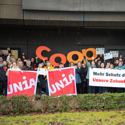 Eine Gruppe Unia-Mitglieder, die bei Coop arbeiten, stehen hinter einem Transparent. Darauf steht «Mehr Schutz dank starkem GAV: Unsere Zukunft, unsere Rechte.». Sie halten Schilder mit Forderungen in die Höhe.