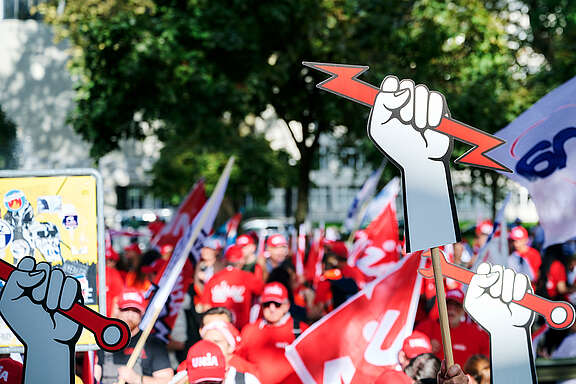 Demonstrant:innen recken an der Abschlusskundgebung Berufssymbole in die Höhe