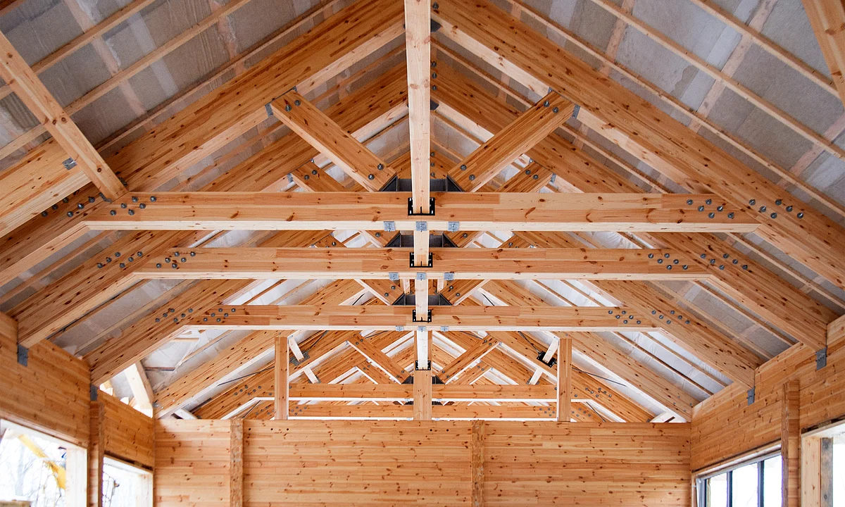 Vista interna di una capriata in legno con travi portanti e giunti visibili, che illustra il lavoro artigianale nella costruzione in legno.