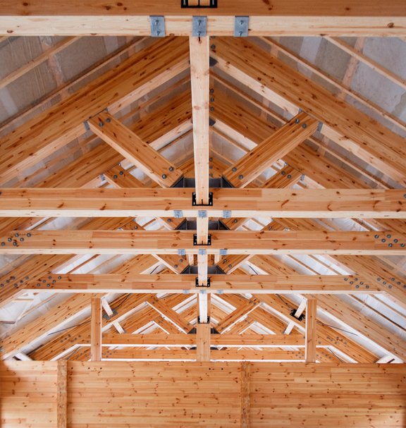 Innenansicht eines Holzfachwerks mit tragenden Balken und sichtbaren Verbindungen, die die handwerkliche Arbeit im Holzbau veranschaulicht.