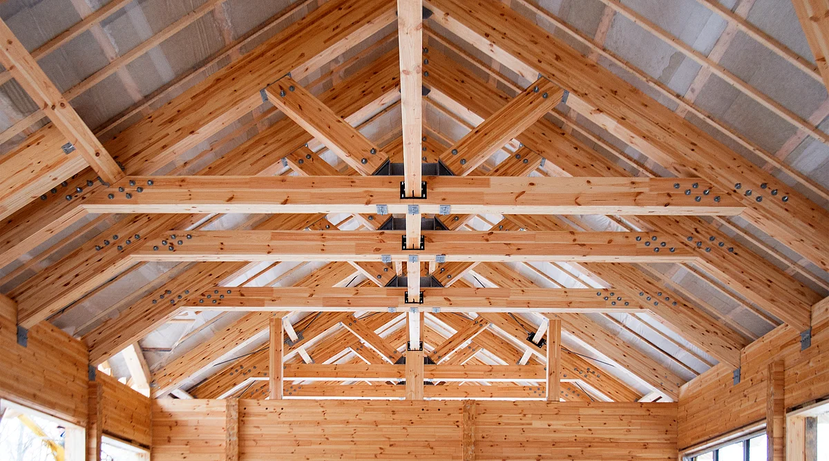 Innenansicht eines Holzfachwerks mit tragenden Balken und sichtbaren Verbindungen, die die handwerkliche Arbeit im Holzbau veranschaulicht.
