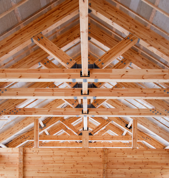 Vista interna di una capriata in legno con travi portanti e giunti visibili, che illustra il lavoro artigianale nella costruzione in legno.