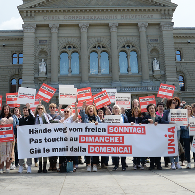 Des vendeuses et vendeurs manifestent devant le Palais fédéral avec des pancartes et une banderole en scandant : «Pas touche au congé du dimanche!»