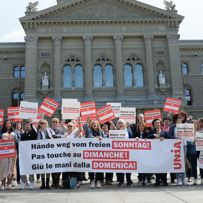 Il personale della vendita manifesta di fronte al Palazzo federale con cartelloni e uno striscione scandendo lo slogan: «giù le mani dalla domenica libera!»