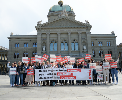 Des vendeuses et vendeurs manifestent devant le Palais fédéral avec des pancartes et une banderole en scandant : «Pas touche au congé du dimanche!»