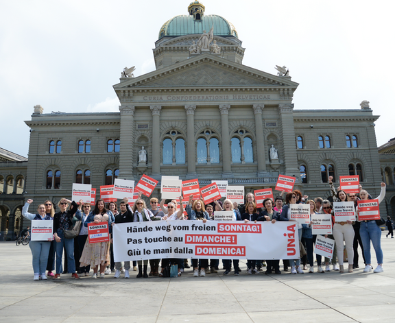 Des vendeuses et vendeurs manifestent devant le Palais fédéral avec des pancartes et une banderole en scandant : «Pas touche au congé du dimanche!»