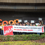 Un groupe de 50 personnes brandissent une banderole, des drapeaux, des pancartes en carton et de grandes lettres découpées inspirées du logo Coop. Ils lèvent le poing en l’air et affichent l’image d’un syndicat combatif. Sur la banderole, on peut lire: «Une meilleure protection grâce à une CCT forte: notre avenir, nos droits.»