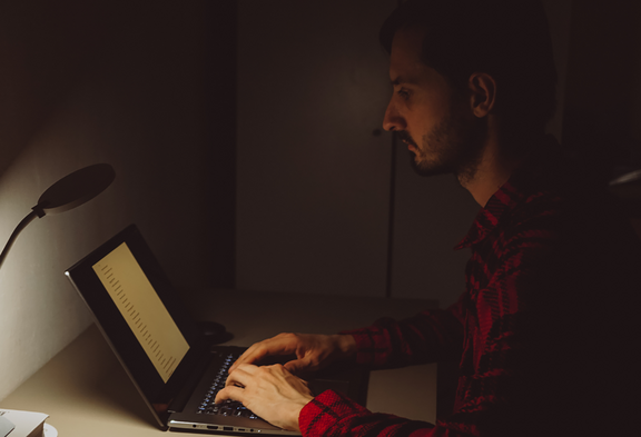 Una persona che lavora da casa: sul tavolo si vedono un computer portatile, un giocattolo, una tazza di caffè iniziata e resti di cibo.