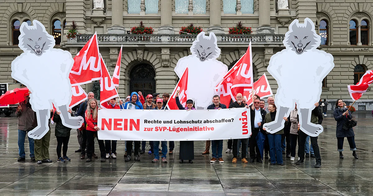 Demonstrierende vor dem Bundeshaus halten ein Banner mit der Aufschrift «NEIN zur SVP-Lügeninitiative» und protestieren mit Unia-Fahnen sowie grossen Figuren von Wölfen im Schafspelz gegen den Abbau von Rechten und Lohnschutz.