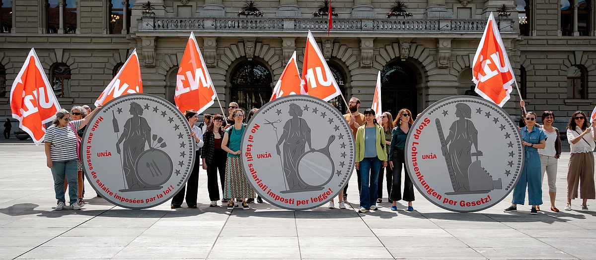 Militanti Unia davanti al Palazzo federale a Berna tengono tre monete giganti raffiguranti Helvetia con la scritta «No ai tagli salariali imposti per legge».
