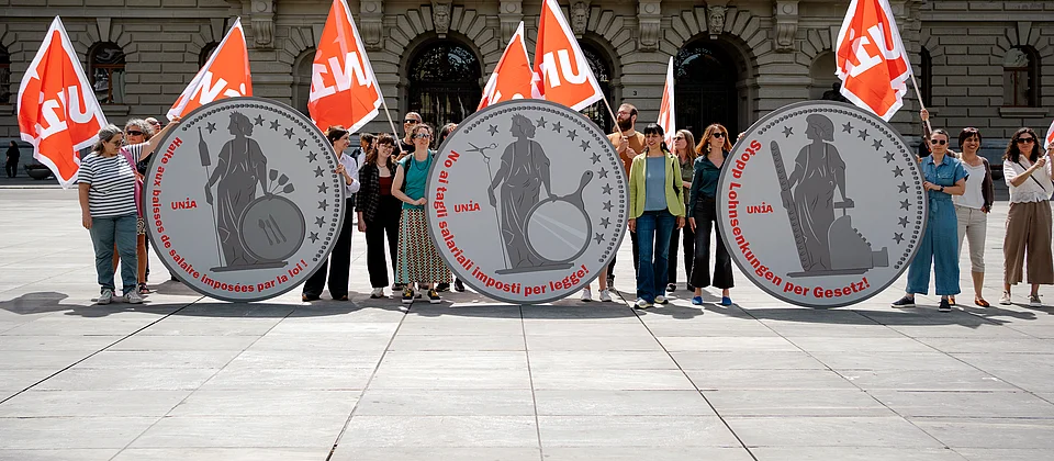 Militanti Unia davanti al Palazzo federale a Berna tengono tre monete giganti raffiguranti Helvetia con la scritta «No ai tagli salariali imposti per legge».