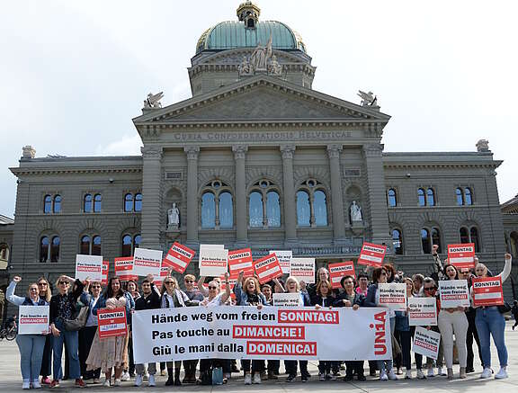 Des vendeuses, des vendeurs et des syndicalistes devant le Palais fédéral à Berne. Ils tiennent une banderole et des affiches. On peut y lire «Pas touche au dimanche!»