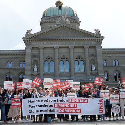 Des vendeuses, des vendeurs et des syndicalistes devant le Palais fédéral à Berne. Ils tiennent une banderole et des affiches. On peut y lire «Pas touche au dimanche!»