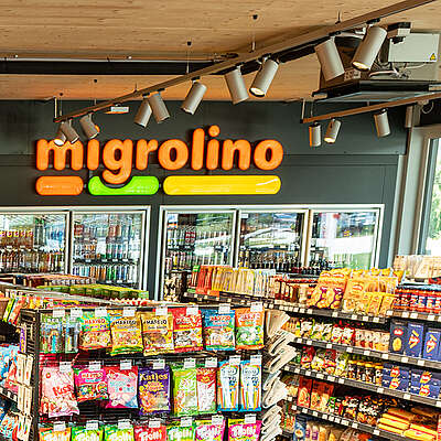 Innenansicht eines Verkaufsgeschäfts. Regale mit verschiedenen Kiosk-Produkten, einigen Lebensmitteln, einem Kühlgestell mit Getränken und einer Kassentheke sind zu sehen.