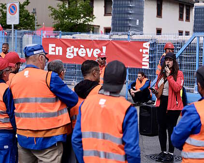 Une syndicaliste d’Unia prend la parole devant un groupe de grévistes en bleu de travail