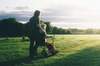Une femme pousse une vieille femme en fauteuil roulant sur une prairie