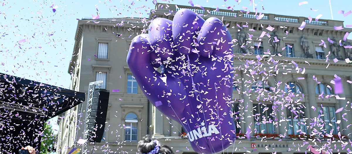 Aufblasbare violette Faust der Gewerkschaft Unia über einer feministischen Demonstration, umgeben von Konfetti vor einem Gebäude in Bern