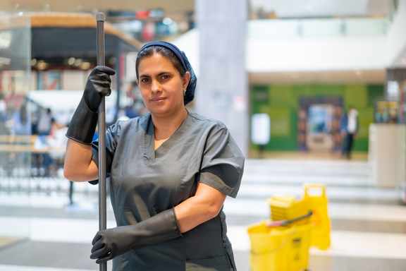 Un’addetta alle pulizie in tenuta da lavoro intenta a pulire il pavimento con un mocio in un centro commerciale. 