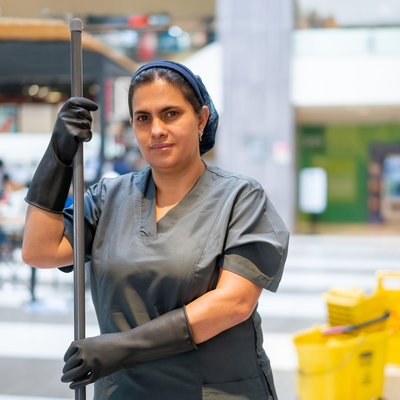 Eine Reinigungsangestellte in Arbeitskleidung steht in einem Einkaufszentrum und hält einen Wischmopp. 