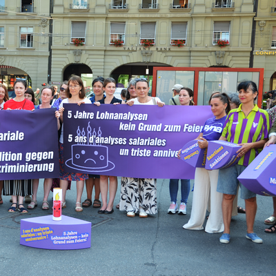 Una trentina di donne appartenenti a diverse organizzazioni progressiste protestano sulla Piazza federale di Berna. Sono in piedi davanti a una gigantesca torta di polistirolo viola. I singoli pezzi di torta simboleggiano le rispettive lacune della legge sulla parità di genere.
