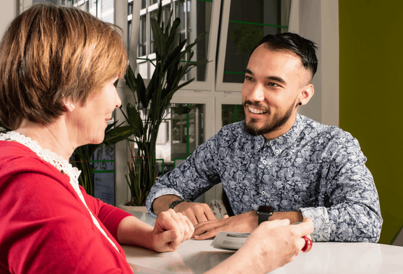 [Translate to Français:] Eine Sachbearbeiterin der Arbeitslosenkasse berät einen Kunden am Schalter