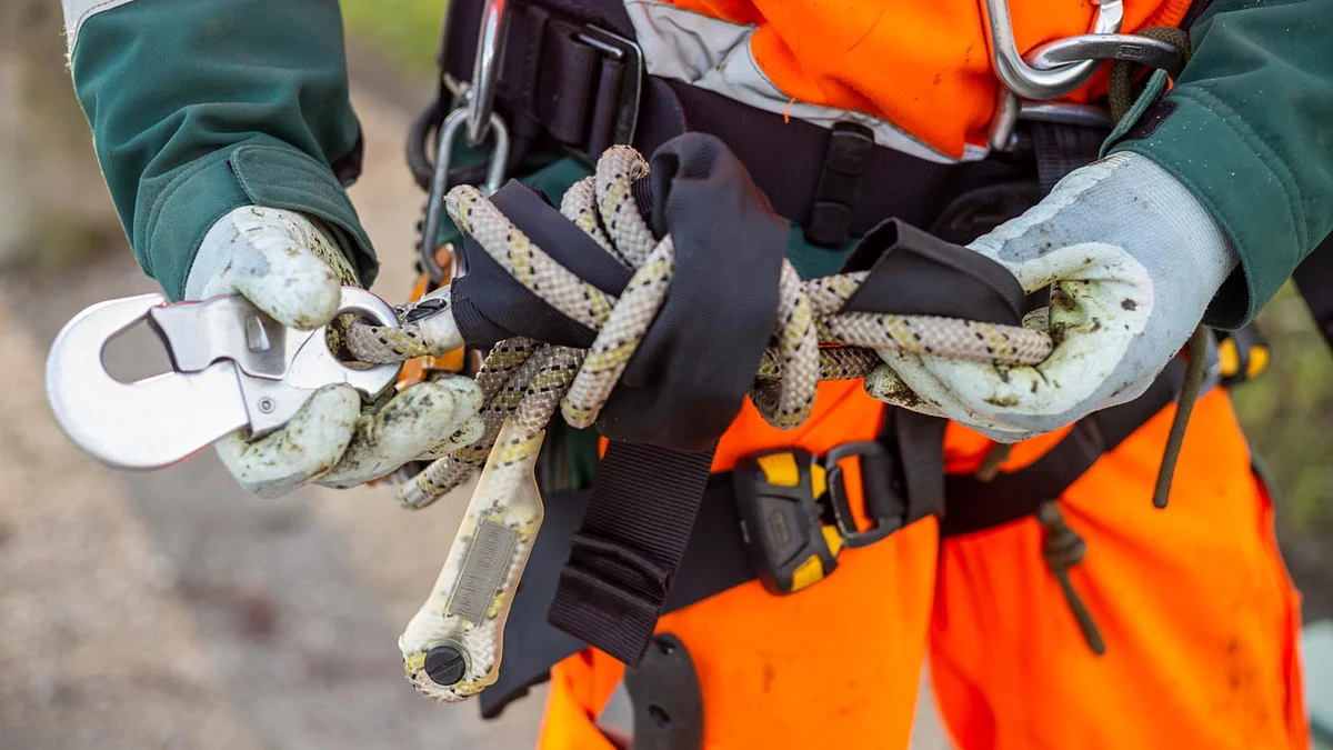 Une personne en tenue de protection tient une corde de sécurité avec un mousqueton. Gros plan sur la sécurité au travail et la protection de la santé.