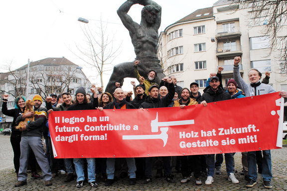 Uomini e donne con il pugno alzato e uno striscione con la scritta: Il legno ha un futuro. Contribuite a dargli forma!