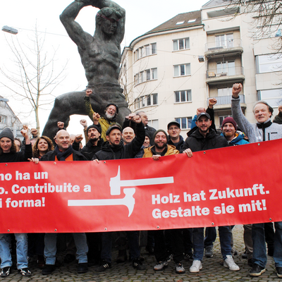Männer und Frauen mit erhobener Faust und einem Transparent mit der Aufschrift: Holz hat Zukunft. Gestalte sie mit! 