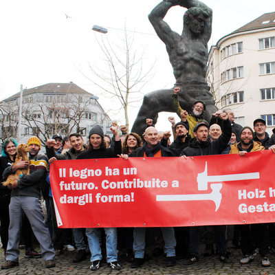 Uomini e donne con il pugno alzato e uno striscione con la scritta: Il legno ha un futuro. Contribuite a dargli forma!